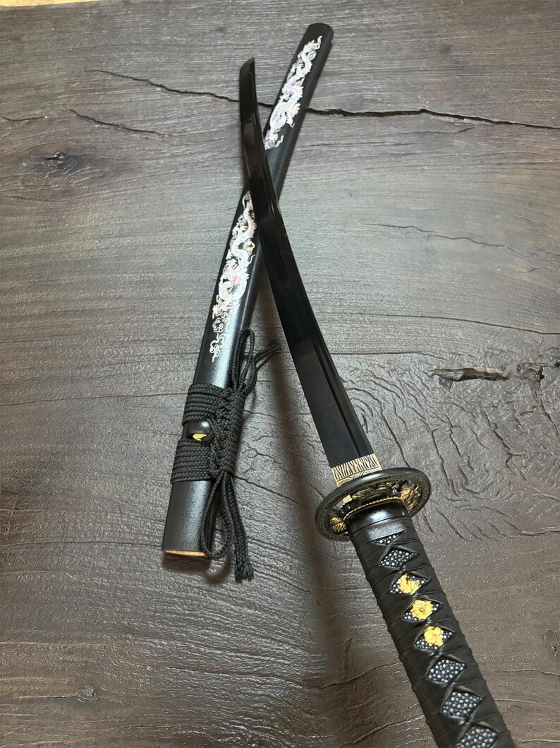 May include: A black katana sword with a decorative handle and scabbard. The scabbard features a white dragon design. The handle is wrapped in black material with gold accents. The blade is black.