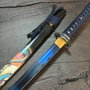 Op de afbeelding: Een Japanse katana-zwaard met een blauw lemmet en een decoratief handvat. De schede is zwart met een kleurrijk slangenontwerp. Het handvat is gewikkeld in blauwe stof met gouden accenten. Het zwaard wordt gepresenteerd op een donker houten oppervlak.