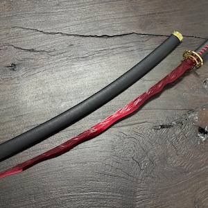 May include: A red and black katana sword with a black scabbard. The sword features a red blade with a wavy design, a black handle wrapped with red cord, and gold accents. The scabbard is black with gold details.