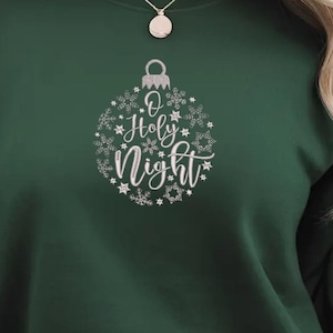 May include: A dark green sweatshirt with a white ornament design that says "O Holy Night".