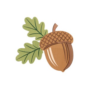 Puede incluir: Una bellota bordada con una tapa y cuerpo marrones, acompañada de dos hojas de roble verdes. La bellota tiene una tapa texturizada y un cuerpo liso con un reflejo beige claro. Las hojas tienen una apariencia detallada y cosida.