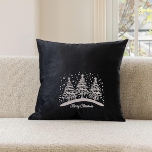 May include: Black throw pillow with a white embroidered design of three snow-covered pine trees and the text "Merry Christmas".
