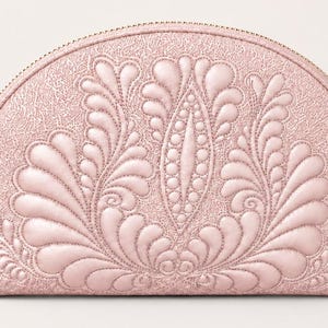 May include: A semi-circular light pink pouch featuring a textured surface and intricate, raised quilted feather patterns. The design includes a central vertical motif surrounded by symmetrical, curved plume shapes, all finished with a gold zipper.