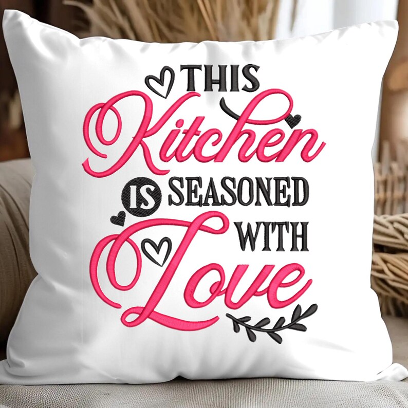 May include: White pillow with pink and black embroidery that reads "This Kitchen is Seasoned with Love".
