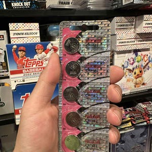 May include: A package of Maxell CR1632 3V lithium coin cell batteries. The batteries are in a clear plastic blister pack with pink backing. The package has holographic foil accents and the Maxell logo.