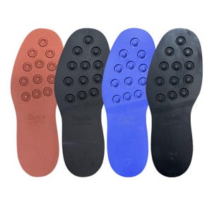 May include: Four shoe soles in shades of red, black, and blue. Each sole has a textured surface with circular patterns and the brand name "Dainite" printed on them. The soles are designed for footwear.