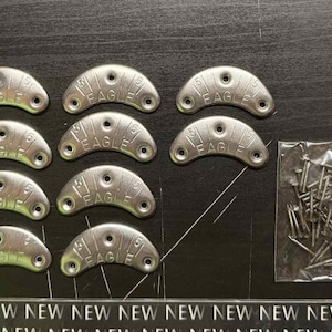May include: Silver tap shoe taps, each stamped with "EAGLE", are displayed alongside a small bag of nails. The taps are arranged on a dark surface. The word "NEW" is repeated along the bottom of the image.
