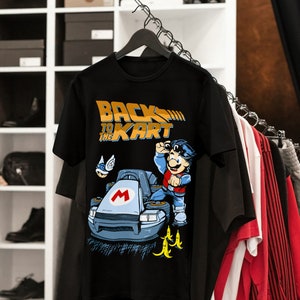 May include: Black t-shirt with a graphic of a cartoon character driving a go-kart. The text "Back to the Kart" is printed in yellow on the shirt.