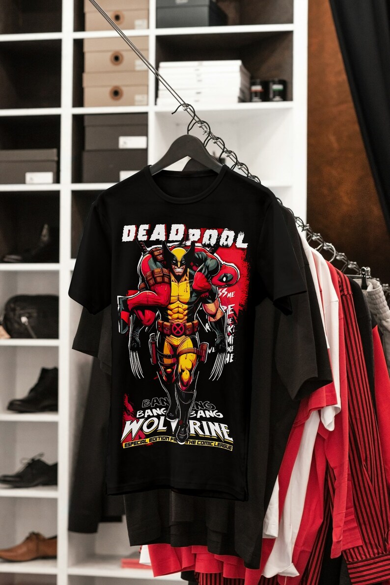 Puede incluir: Camiseta negra con un gr&aacute;fico de Wolverine cargando a Deadpool. El dise&ntilde;o incluye las palabras "DEADPOOL" y "WOLVERINE" en blanco y rojo, con texto adicional en la parte inferior. La camiseta est&aacute; colgada en una percha con otras prendas.