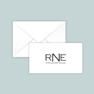 May include: A white rectangular business card featuring the black serif monogram RNE centered above the text RYAN EDWARD NELSON, positioned in front of a matching white envelope with a triangular flap closure.