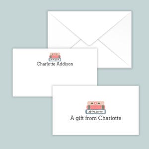 May include: White stationery set featuring two rectangular cards and one envelope. Each card displays a stack of three books in pink and blue with a floral detail, accompanied by the printed text Charlotte Addison or A gift from Charlotte.