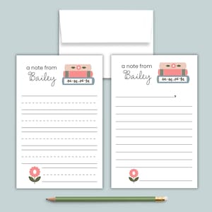May include: Two white stationery sheets with the text a note from Bailey, featuring a stack of three books and a pink flower graphic. One sheet has primary-style dashed writing lines, the other has solid lines. A plain white envelope and green pencil.