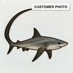 May include: A sticker featuring a detailed illustration of a shark in shades of gray and white. The shark has a curved tail and prominent fins. The text "CUSTOMER PHOTO" is in a white rectangle at the top.