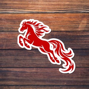 Könnte beinhalten: Ein roter Pferdesticker mit weißem Umriss, der mit fließender Mähne und Schweif springt. Der Aufkleber befindet sich auf einer Holzoberfläche. Das Pferdedesign ist eine stilisierte Illustration.