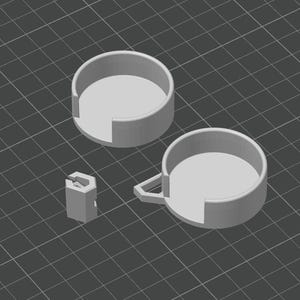 May include: A 3D-rendered image of three light gray objects. Two are circular with a cutout section, resembling coasters. The third is a small, hexagonal piece. All objects are on a dark gray grid background.