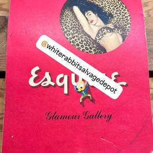 Op de afbeelding: Een rode kaart met het woord "Esquire" in witte letters en de woorden "Glamour Gallery" in zwarte letters. De kaart toont een cirkelvormige afbeelding van een vrouw in een bikini met luipaardprint die op een achtergrond met luipaardprint ligt.