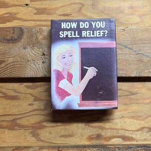 May include: A vintage card game with a cartoon illustration of a woman writing on a chalkboard. The text on the card reads "How do you spell relief?"