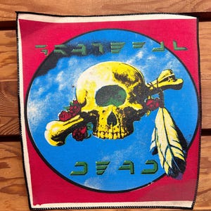 May include: A red, white, and blue patch with a skull and crossbones design. The skull is yellow with green eyes and a white bone. The text "GRATEFUL DEAD" is written in a stylized font.