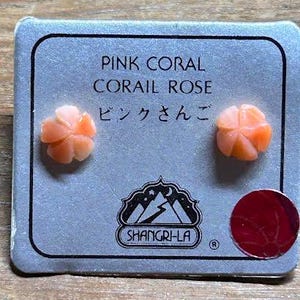 K&ouml;nnte beinhalten: Ein Paar rosa Korallenohrstecker auf einer grauen Karte. Auf der Karte steht "PINK CORAL CORAIL ROSE" und japanischer Text. Die Ohrringe sind bl&uuml;tenf&ouml;rmig und haben eine hellorange Farbe. Die Karte hat auch ein Logo und einen roten Aufkleber.