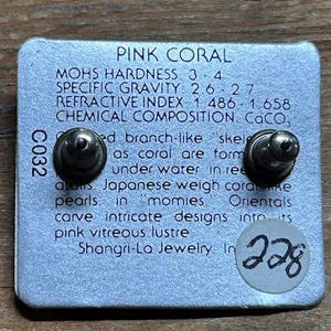 K&ouml;nnte beinhalten: Eine silberne Ohrringkarte mit zwei Ohrsteckern. Die Karte tr&auml;gt den Text "PINK CORAL" und Details &uuml;ber die Eigenschaften der Koralle. Ein kleiner Aufkleber mit der Nummer "228" befindet sich auf der Karte.