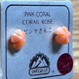 K&ouml;nnte beinhalten: Ein Paar rosa Korallenrosen-Ohrstecker auf einer grauen Karte. Auf der Karte steht "PINK CORAL CORAIL ROSE" und japanische Schriftzeichen. Die Ohrringe sind hellorange und rosenf&ouml;rmig.