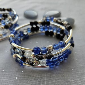 May include: A multi-strand bracelet with blue, clear, and black beads. The bracelet is made with silver metal wire and has a silver metal bead accent.