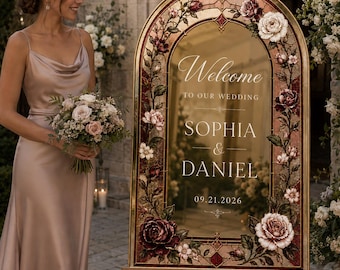May include: An arched wedding welcome sign featuring a gold-toned mirror surface framed by a decorative border of painted red and white roses. The text reads Welcome to our wedding, Sophia & Daniel, and the date 09.21.2026 in white lettering.