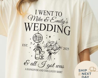 May include: Cream-colored t-shirt with black text that reads "I WENT TO Mike & Emily's WEDDING" with a graphic of a disco ball, flowers, and a champagne bottle. The text "& all I got was A HANGOVER AND THIS LOUSY SHIRT" is also printed on the shirt.