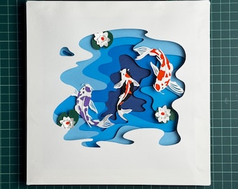 May include: A square canvas artwork with a layered paper design of a koi pond. The pond is in shades of blue, with three koi carp in orange, black, and purple. White lily pads with red centres are also present.