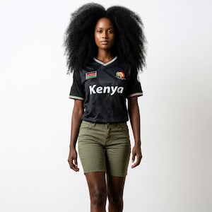 Può includere: Una maglia nera a maniche corte con la scritta Kenya in bianco sul petto, una toppa con la bandiera del Kenya, un emblema circolare e bordini rossi, bianchi e verdi sullo scollo a V e sulle maniche, abbinata a pantaloncini color oliva.
