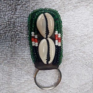 Könnte beinhalten: Ein grüner, schwarzer, weißer und roter Perlen-Schlüsselanhänger mit zwei Kaurischnecken und einem silbernen Ring.