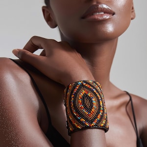 Könnte beinhalten: Ein breites Manschettenarmband mit aufwendigen Perlenarbeiten in einem sich wiederholenden augenförmigen Muster. Das Design umfasst eine Palette aus dunkelbraunen, orangen, gelben und hellblauen Glasperlen, die in konzentrischen Reihen angeordnet sind.