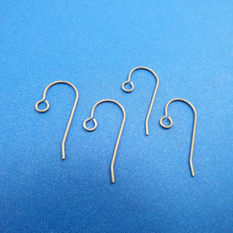 May include: Four silver earring hooks on a blue background. The hooks are made of metal and have a simple design.