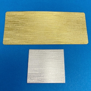 May include: Two rectangular pieces of textured paper. The top piece is gold and the bottom piece is silver.