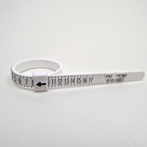May include: White plastic ring sizer with black markings for sizes 5 to 17. The sizer has a black arrow and the text "PAT. PEND. 9101693".