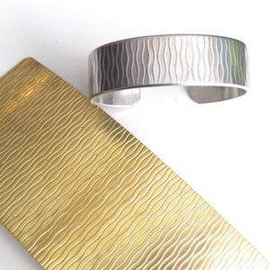 May include: A silver metal bracelet with a wavy pattern. The bracelet is next to a sheet of brass with a similar wavy pattern.