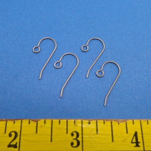 May include: Three silver earring hooks, measuring approximately 1 inch in length, are displayed on a blue surface with a yellow measuring tape in the foreground.