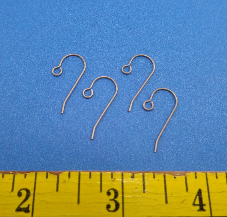 May include: Three silver earring hooks, measuring approximately 1 inch in length, are displayed on a blue surface with a yellow measuring tape in the foreground.