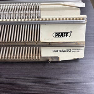 May include: A vintage Pfaff Duomatic 80 knitting machine, cream and silver in colour. The machine has the Pfaff logo and the text "system PASSAP swiss made". The serial number 3054334 is visible.