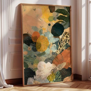 May include: Abstract art print in a gold frame. The artwork features a colourful composition of organic shapes in shades of yellow, orange, green, and blue. The painting has a textured appearance, with visible brushstrokes and layered colours. The artwork is leaning against a white wall.