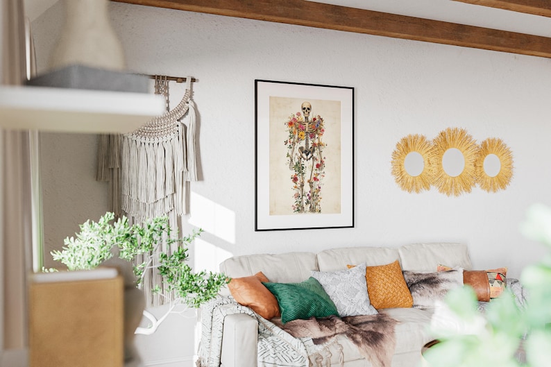 May include: A framed print featuring a skeletal figure adorned with colorful flowers. The artwork hangs above a white sofa with decorative pillows and a faux fur throw. Three round, woven wall mirrors are also visible.
