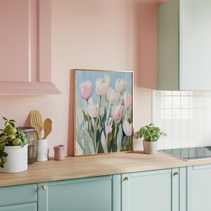 May include: A framed painting of pink and white tulips with green leaves on a light blue background. The painting is hanging on a pink wall in a kitchen.
