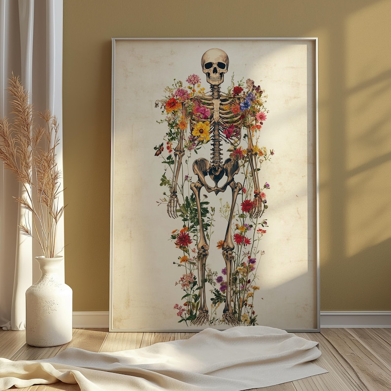 May include: A framed print featuring a human skeleton adorned with colorful flowers. The artwork has a vintage aesthetic, with the skeleton's bones and the flowers' vibrant hues contrasting against a cream-colored background. The print is displayed in a room with natural light.
