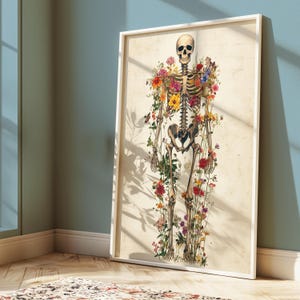 May include: A framed art print featuring a human skeleton adorned with colorful flowers. The artwork has a vintage aesthetic, with the skeleton's bones and the flowers in full bloom. The frame is white, and the background is a light beige.