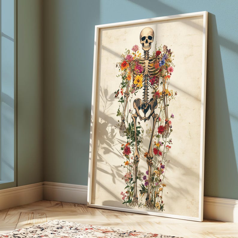 May include: A framed art print featuring a human skeleton adorned with colorful flowers. The artwork has a vintage aesthetic, with the skeleton's bones and the flowers in full bloom. The frame is white, and the background is a light beige.
