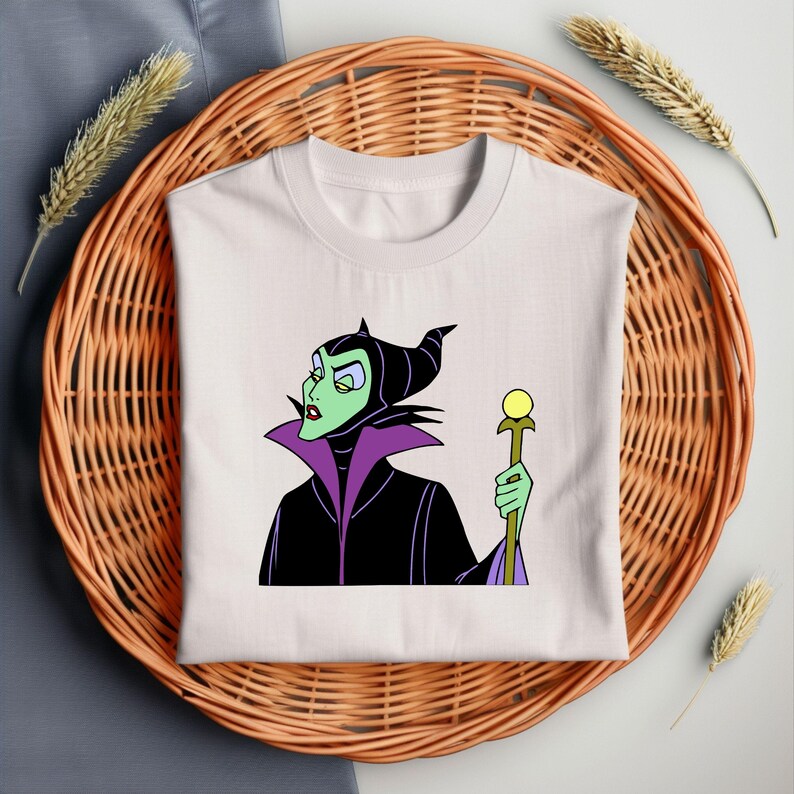 Puede incluir: Camiseta blanca con una imagen de dibujos animados de Mal&eacute;fica de La Bella Durmiente de Disney. Lleva un vestido negro y morado y sostiene un bast&oacute;n con un orbe amarillo en la parte superior.
