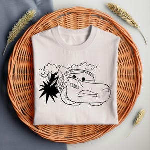 Puede incluir: Una camiseta blanca con un dibujo en blanco y negro de un coche de carreras de dibujos animados con el n&uacute;mero 95 en el lateral. El coche est&aacute; en una nube de humo y tiene una expresi&oacute;n de sorpresa en su rostro.