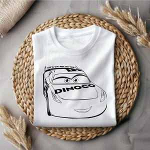 Puede incluir: Camiseta blanca con una ilustraci&oacute;n en blanco y negro de un coche de carreras de dibujos animados con la palabra "Dinoco" en el lateral.