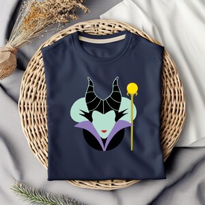 Puede incluir: Una camiseta azul marino con un gr&aacute;fico de Mal&eacute;fica de La Bella Durmiente de Disney. El gr&aacute;fico presenta la cara de Mal&eacute;fica, sus cuernos y un collar morado, con un bast&oacute;n dorado y un orbe amarillo en la parte superior.