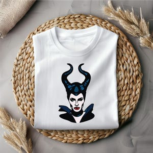 Puede incluir: Camiseta blanca con un gr&aacute;fico negro y azul de Mal&eacute;fica de la pel&iacute;cula de Disney "La Bella Durmiente".